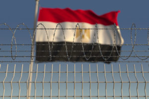 Blurred waving flag of Egypt behind barbed wire fence. 3D rendering (Shutter Stock/Novikov Aleksey)