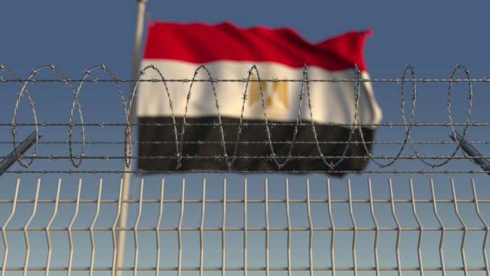 Blurred waving flag of Egypt behind barbed wire fence. 3D rendering (Shutter Stock/Novikov Aleksey)